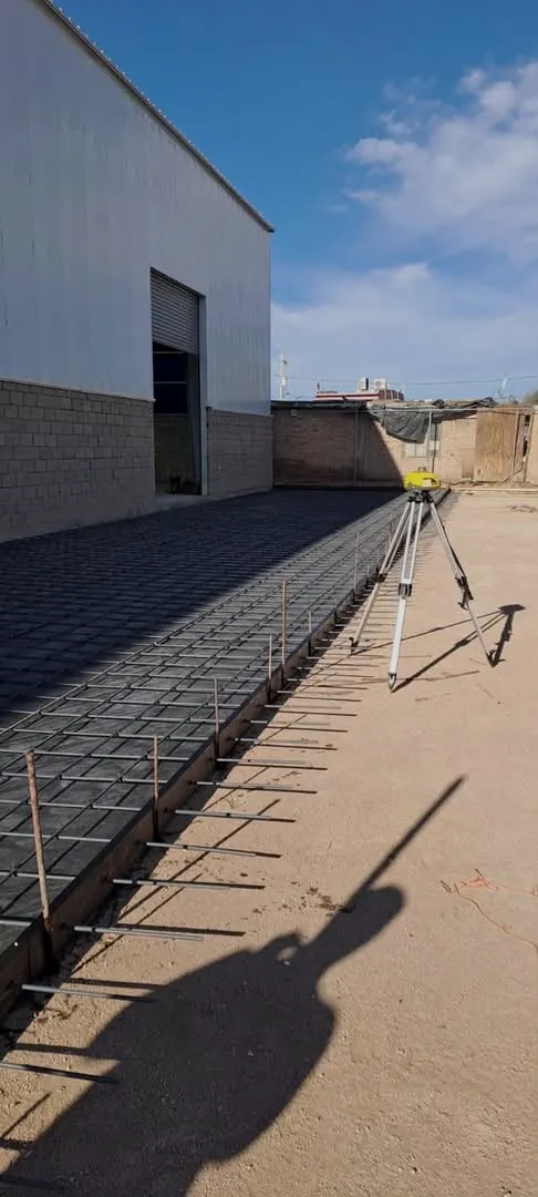 Nivel láser sobre tripié junto a armado de malla de acero antes del colado
